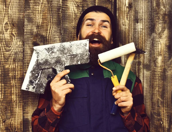 Homem construtor barbudo segurando várias ferramentas de construção com rosto feliz — Fotografia de Stock