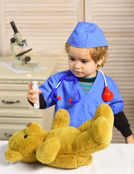 Niño en uniforme quirúrgico sostiene jeringa sobre fondo de madera. —  Fotos de Stock