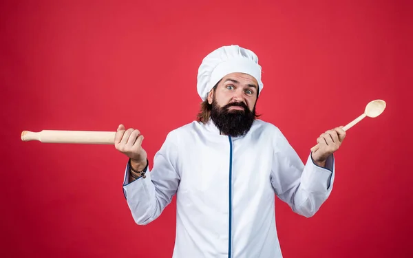 Concept van huishouding. Een volwassen man met een baard draagt een koksmutje. mannelijke kok klaar voor het bereiden van voedsel. brutale hipster in schort gaat koken. Etenstijd. Ik weet niet wat ik hiermee moet. — Stockfoto