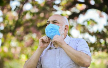 Önceden uyarılmış demek korunmak demektir. Coronavirus kapanışı sırasında hayat. Hastalık korkusu. Virüsle savaşma stratejisi. Halka açık yerleri ziyaret etmek yasak. Tıbbi maskeli kıdemli adam. Parktaki çiçek ağacı.