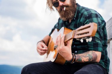 Kareli gömlekli sakallı adam şarkı söylüyor. Müzisyen müzisyen. müzik teli enstrümanı. Olgun karizmatik erkek gitarist. Sakallı ve bıyıklı adam gitar çalıyor. Sigara kötüdür.