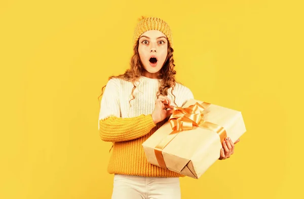 Niño mantenga presente caja de fondo amarillo. regalo de Navidad venta de compras. Que tu navidad sea brillante. Felices vacaciones de invierno. pequeña niña sorprendida de punto sombrero y suéter. Feliz Navidad. — Foto de Stock