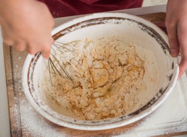 Çocuk çırpılmış yumurta ve un çırpıyor hamur yapmak için çırpıyor, pişiriyor