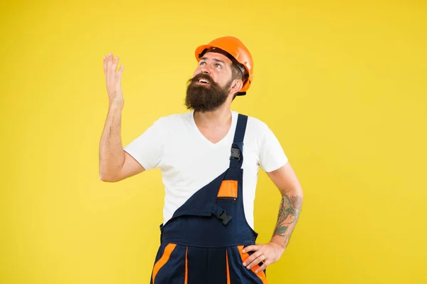Construtor barbudo em chapéu duro e uniforme de trabalho olhar para cima fundo amarelo, construção — Fotografia de Stock