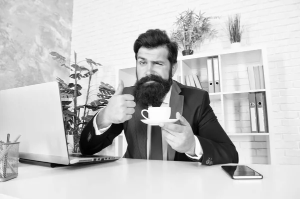La mejor manera de disfrutar del café. Hombre barbudo mostrar pulgares hasta la taza de café. El hombre de negocios bebe café en la oficina. Descanso. Bebida caliente. Té de desayuno. Bebida de la mañana. Placeres simples — Foto de Stock