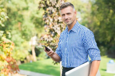 Çevik iş. Modern cihazlarla iletişim. Her zaman çevrimiçi kal. Neşeli adam cep telefonuyla konuşuyor. Yakışıklı iş adamının saçları beyazlamış. olgun adam bilgisayar taşır