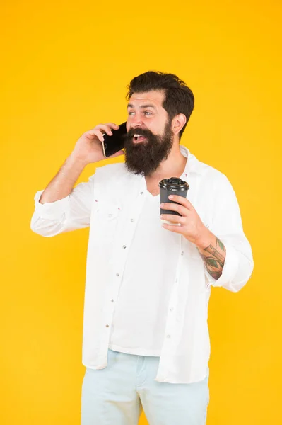 Glad skäggig man som pratar i telefon medan han dricker kaffe. Brutalt hipster dricker hämtmat från muggen. Killen med skägg och mustasch har mobilsamtal. morgonrutin — Stockfoto