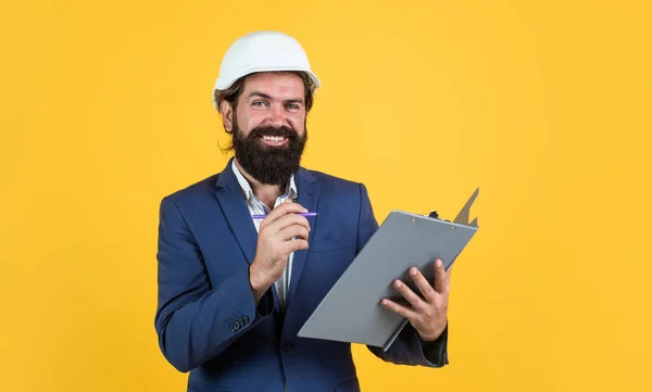Boldog szakállas férfi kemény kalapban az építési területen dokumentumok, építész — Stock Fotó