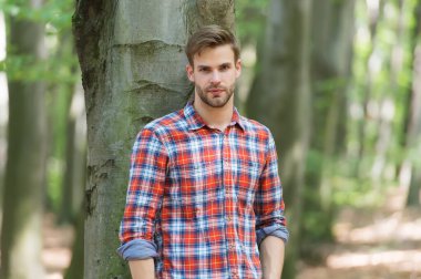 Mükemmel saçlar. Sıradan moda tarzı. Ormandaki kaslı adam. Açık havada düğmesiz gömlekli seksi maço. Genç traşsız adam saçını taramış. Erkek güzellik ve moda. Tüylü adam kareli gömlek giyiyor.
