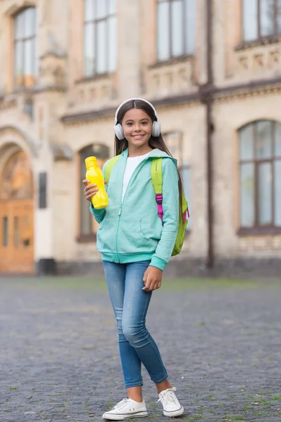 Flicka dricka vatten vård kropp hydratisering med juice flaska i hörlurar på skolgården, hälsovård i barndomen — Stockfoto