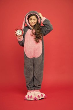 Sabah alarmı. Tavşan çocuk kırmızı arka plan. Yavru hayvan. Zamanı sayıyorum. Sıradan bir gün başlıyor. Sevimli tavşancık alarm saatini tut. Tavşan kostümlü küçük kız. Çocuk tavşan kigurumi. Kız tavşanlı pijama