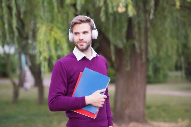 Öğrenci kitaptan bilgi alıyor. Elderning konsepti. Adam kulaklıkla müzik dinliyor ve not defterini tutuyor. Kulaklıklı yakışıklı adam parkta rahatlıyor. modern yaşam eğitim teknolojisi