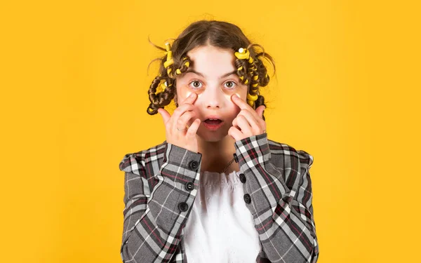 Κομμωτήριο. Κορίτσι με μπικουτί και κλιπ μαλλιών στα μαλλιά της σε κίτρινο φόντο. Κοριτσάκι κατσαρό γύρω από τα μαλλιά της. Δημιουργήστε όμορφο χτένισμα. Υπέροχο χτένισμα. Ευτυχισμένο παιδί με μπαλώματα ματιών — Φωτογραφία Αρχείου
