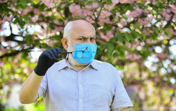 Amati tindakan pencegahan saat pandemi. hidup sehat. memakai topeng di taman sakura merah muda mekar. Pria di sakura dengan topeng pelindung. Bau bunga mekar pada karantina coronavirus — Stok Foto