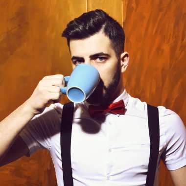 Sakallı adam ciddi bir yüzle bir fincan çaydan içiyor.