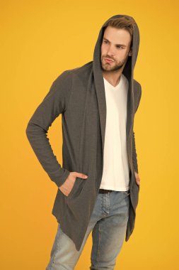 Sportif tarzda. Günlük yaşam için rahat kıyafetler. Moda adamı sarı arka plan. Moda bakışı. Yakışıklı adam kapüşonlu şık bir manto giyiyor. Erkekler için günlük kıyafet. Moda trendleri. Gençler için modern kıyafetler