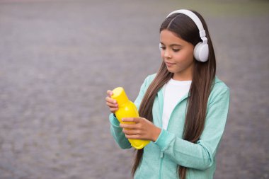 Kulaklıklı çocuk susuzluktan, sağlıklı yaşam tarzından dolayı içmek için su şişesini açıyor.
