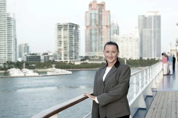 Vrouw glimlach in zakelijke jas aan boord in Miami, VS. Sensuele vrouw aan boord aan de skyline van de stad. Mode, schoonheid, kijk. Reizen voor zaken. Wanderlust, avontuur, ontdekking, reis — Stockfoto