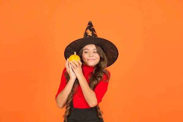 Funny girl in witch costume hat for Halloween with pumpkin or squash on orange background, halloween food — Stock Photo, Image