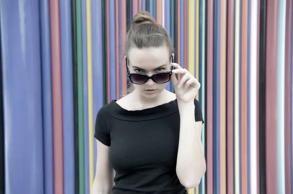 Divat városi stílus koncepció. Egy titokzatos hölgy, aki fekete szemüveget visel egy csíkos színes fal előtt Párizsban. Nő elegáns megjelenés divatos ruhát. Nagyvárosok városi divatja — Stock Fotó