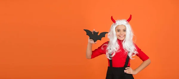 Happy kid on Halloween wear funny carnival costume and horns indoor holding small bat, trick or treat. copy space — Stock Photo, Image