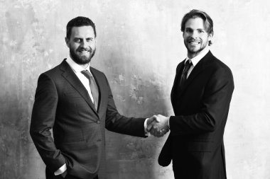 Ceketli mutlu adamlar el sıkışırken el ele tutuşuyorlar.