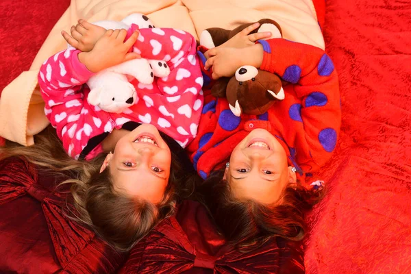 Kids in pajamas hug teddy bears on red background — Stock Photo, Image