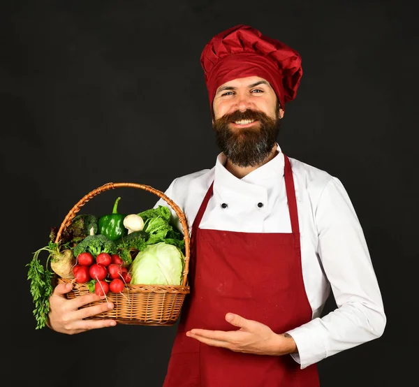 Koch mit Lächeln in weinrotem Hut und Schürze hält Gemüse — Stockfoto