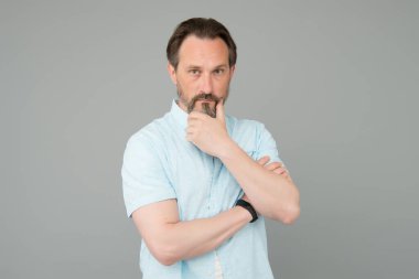 Ciddi ve düşünceli. Olgun bir adamın ciddi bakışları. Sakallı adam gri arka plan olduğunu düşünüyor. Odaklan. Berber dükkanı. Sakallı berber. Berberlik ve tımar. Kaliteli saç kesimi