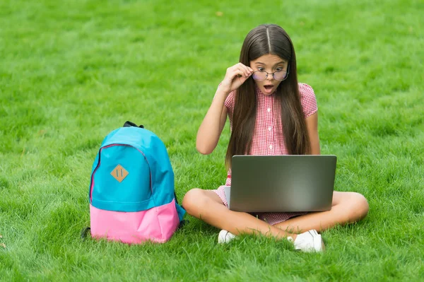 Έκπληκτο παιδί με γυαλιά κοιτάζοντας την οθόνη, ενώ παίζει το παιχνίδι του υπολογιστή στο laptop στο πάρκο, παιδική διασκέδαση — Φωτογραφία Αρχείου