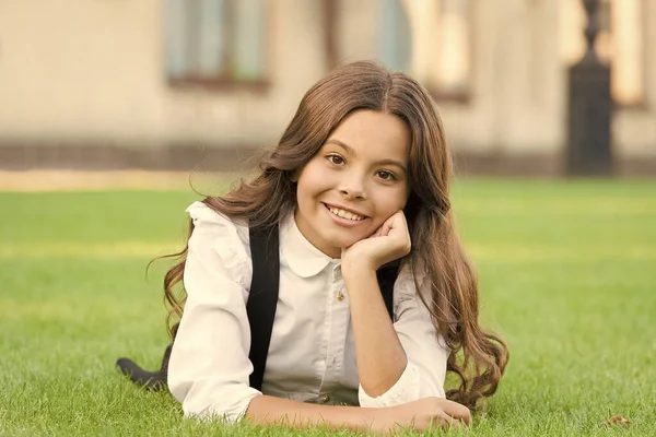 Bienestar mental. Chica uniforme escolar disfrutar de relajarse. Importancia de la relajación. Pequeña colegiala. Relájate en el patio del colegio. Niño relajándose al aire libre. Vacaciones escolares para descansar. Adorable alumno. Niña poniendo césped —  Fotos de Stock