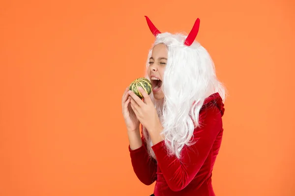 Sólo pasando el rato. Feliz Halloween chica del diablo. infancia. niño hambriento en cuernos de alcahuete. niño tiene el pelo blanco morder calabaza. Jack o Linterna. fiesta de disfraces de carnaval. truco o trato. celebrar las fiestas —  Fotos de Stock