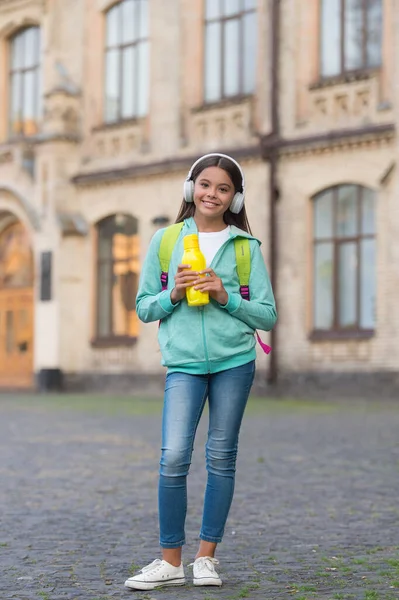 Hälsa återfuktning för barn med vattenflaska lyssna musik i hörlurar och bära skolan ryggsäck utomhus, sport och fitness — Stockfoto