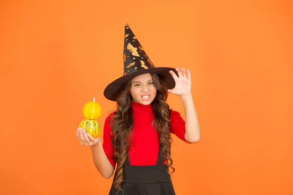 Happy child with long hair wear witch hat hold pumpkin for jack o lantern at autumn holiday celebration, halloween traditional food — Stock Photo, Image