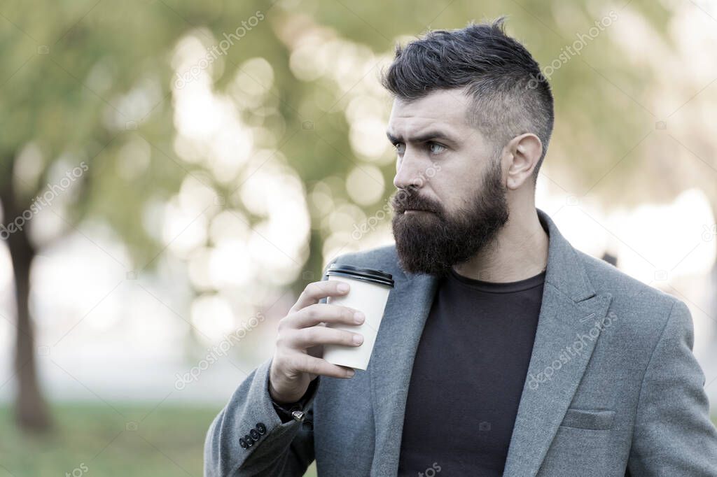 Man bearded hipster prefer coffee take away. Businessman drink coffee outdoors. Reloading energy. Relaxing coffee break. Hipster hold paper coffee cup and enjoy nature environment. Drink it on the go