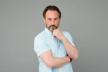 Ciddi görünümlü sakallı olgun bir adam. Gri sakallı, sıradan moda tarzı gri arka planda, tıraş olmamış.