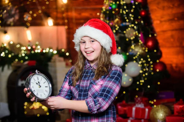 Estoy esperando. Santa Claus niña. Niña con sombrero rojo. Espera a Santa Claus. En Navidad. Santa Claus. Niño elfo con reloj. Árbol de Navidad. Feliz año nuevo. Santa Claus, por favor ven. — Foto de Stock