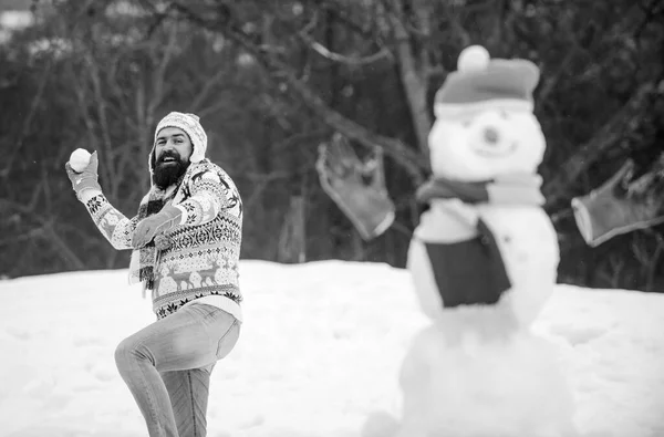 Snow games. Leisure on fresh air. Have fun winter day. Let it snow. Snowman and cheerful bearded hipster knitted hat and warm gloves play with snow outdoors. Christmas holidays. Active lifestyle