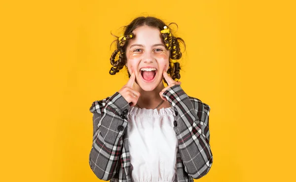 Menina com encrespadores e grampos de cabelo em seu cabelo no fundo amarelo. Penteado lindo. Criança feliz com manchas nos olhos. Raparigas enroladas à volta do cabelo. Criar penteado bonito. Salão de cabeleireiro — Fotografia de Stock