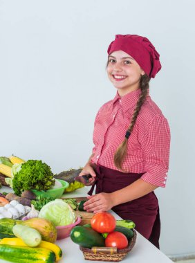Yeni hobisi. Taze çiğ sebze. Yemek zamanı. Mutlu çocuk mutfakta yemek yapıyor. Sadece sağlıklı ve organik yiyecekler. Vitamin dolu. Çocuk şef üniforması ve şapka giyiyor. Genç kız yemek hazırlıyor.