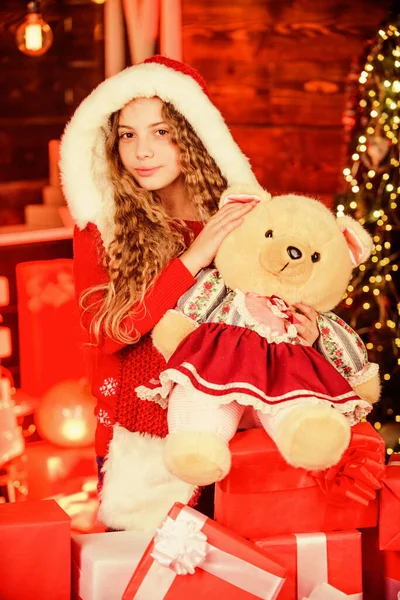 Venta de compras de invierno en la tienda infantil. Niña feliz en el árbol de Navidad. decorar el hogar con alegría. humor de Navidad. celebración de vacaciones familiares. Feliz año nuevo. Santa Kid con caja actual y oso de juguete — Foto de Stock