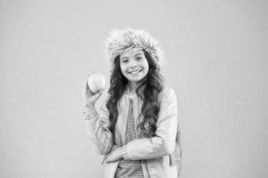 Kış döneminin sonu. Tatil ve tatil. Çocuk pembe arka plan. gençlik gündelik hayatı. Ders sonrası kitapları olan mutlu ve eğitimli bir kız öğrenci. Okul tatili. Küçük mutlu kız kulaklı şapka elma yer.