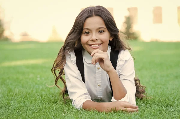 Feliz aluno sorridente. Menina bonito garoto que coloca grama verde. Miúdo feliz a relaxar ao ar livre. Uniforme da escola menina desfrutar relaxar. Aluna alegre. Relaxe no pátio da escola. Boa noite. Intervalo escolar para descanso — Fotografia de Stock