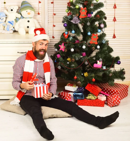 Kerl mit Hut und Schal sitzt am Weihnachtsbaum — Stockfoto