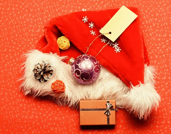 Santa klobouk s vánoční dárkovou krabicí. Udržujte rodinné tradice. Vánoční dárky od Santy. Atributy zimních prázdnin. Nový rok a vánoční ozdoby. Santa klobouk červené pozadí horní pohled — Stock fotografie