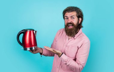 Bunu seviyor. Elektrikli ev aleti. Sakallı adam kırmızı elektrikli su ısıtıcısı kullanıyor. Erkek ev idaresi konsepti. Sıcak suya ihtiyacım var. Adam çay ya da kahve içecek. Bıyıklı ve sakallı vahşi adam.