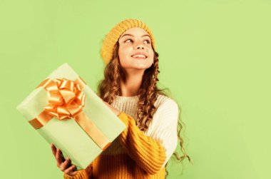 Çocuk hediye kutusunu tut. Alışveriş merkezi konsepti. Doğum günü kutlaması fikri. Keyfin yerinde. Doğum günü geleneği. İyi tatiller. Neşeli küçük kız örgü şapka ve kazak örüyor. Doğum günü sürprizi