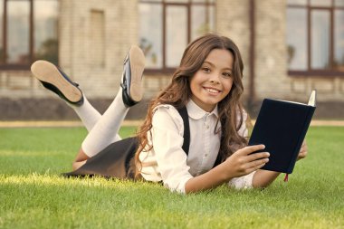 Bilgiye erişim. Temiz hava dersi. Dışarıda kitap okuyan şirin küçük bir çocuk. Eğitici kitap. Çocuklar için edebiyat. Okul üniforması en sevdiği kitapla çimlerin üzerinde yatıyor. Kitap kurdu kavramı