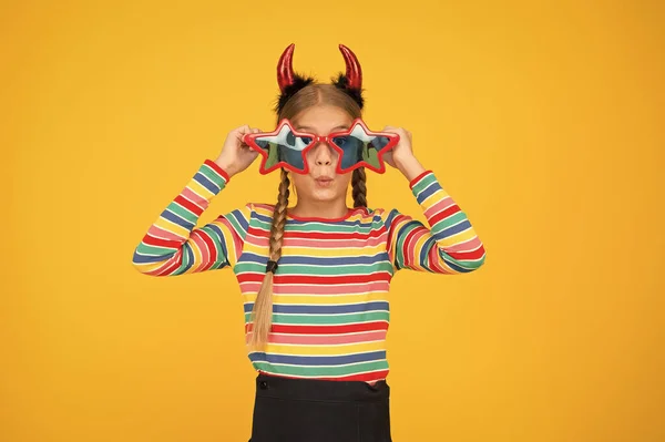 Crazy is her name. Crazy halloween child yellow background. Party girl with crazy look. Fashion kid wear red devil horns and star shaped glasses. Crazy holiday mood. Holiday season. Fancy beauty