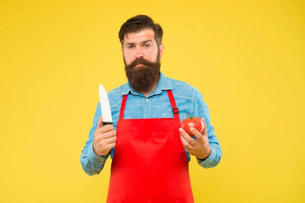 Szakállas férfi szakács friss piros paradicsom segítségével éles kés sárga háttér, konyha — Stock Fotó
